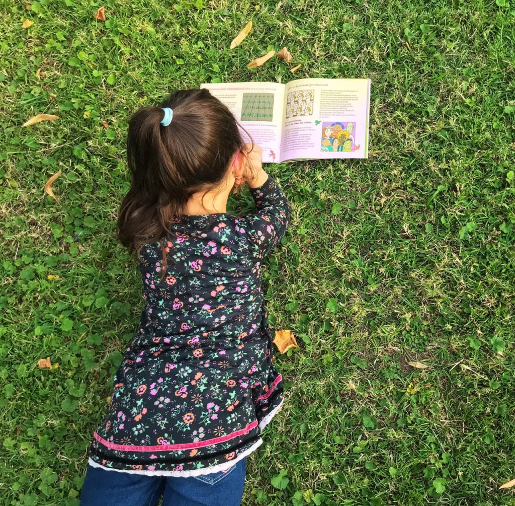Niña leyendo un libro de chirimbote en el pasto.