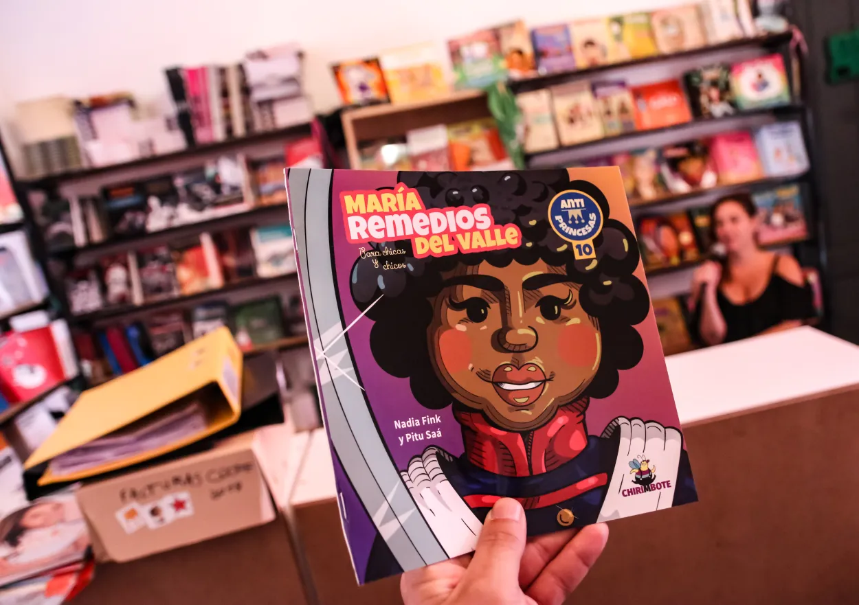 La foto es de una mano mostrando el libro de María Remedios del Valle de la editorial Chirimbote, en el fondo una biblioteca.