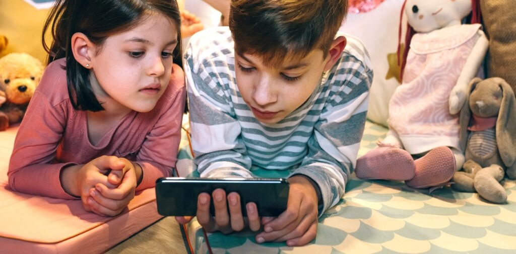 Dos niños mirando una pantalla de celular rodeado de juguetes.